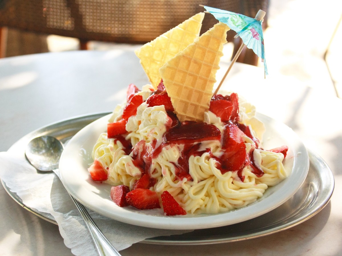 Spaghetti-Eis selber machen: Spaghetti-Eis angerichtet auf einem weißen Teller, garniert mit frischen Erdbeeren und Eiswaffeln.