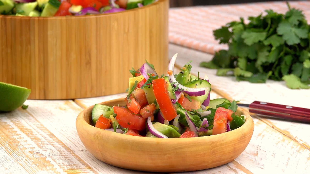 Eine Holzschale mit Guacamole-Salat. Im Hintergrund ein Bund Koriander und eine gro0e Schüssel mit Salat.