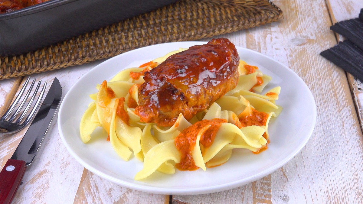 Ein Mini-Hackbraten mit Soße und Nudeln auf einem weißen Teller. Daneben lieggt Besteck.