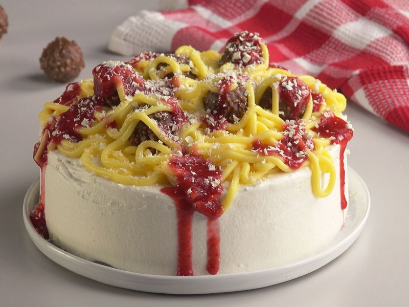 Eine süße Spaghetti-Torte mit Nudeln aus Pudding, Erdbeersoße und Rocher als Fleischbällchen.