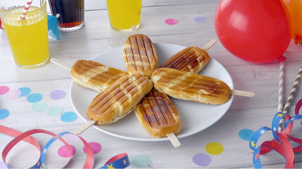 6 Milchbrötchen am Stiel, die sternförmig auf einem Teller liegen. Daneben stehen Gläser mit Limonade, Partydekorationen und ein roter Luftballon.