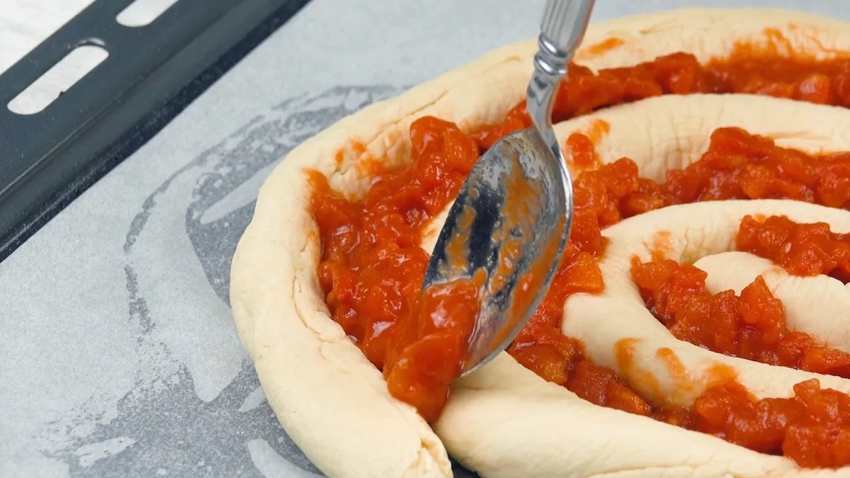 Pizzaspirale wird mit TomatensoÃŸe bestrichen