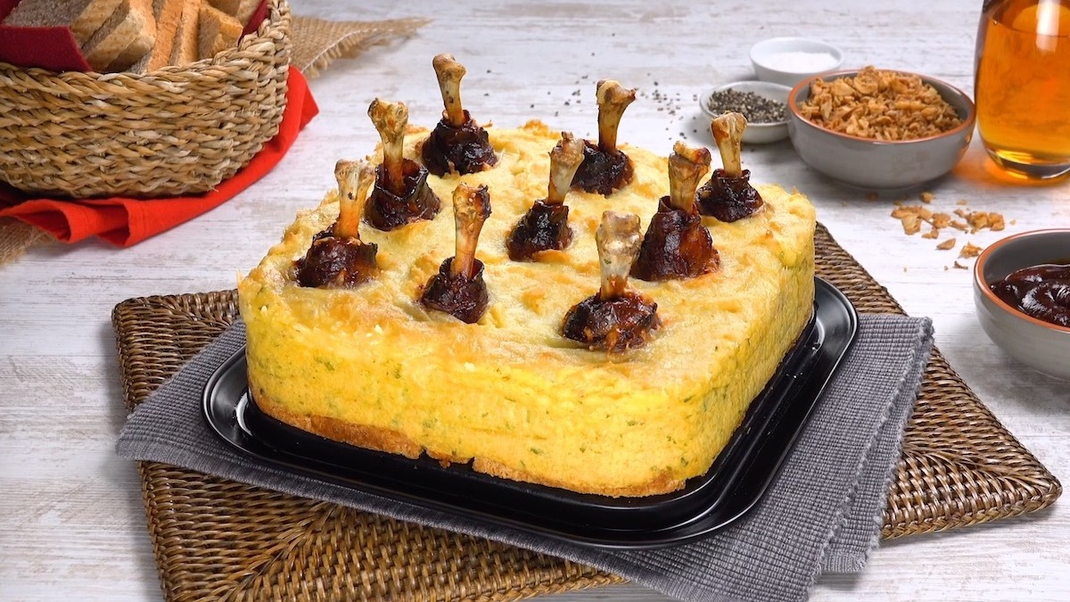 Ein Hähnchenkeulen-Kuchen, daneben ein Korb Brot, eine Schale mit Röstzwiebeln und eine mit Dip.