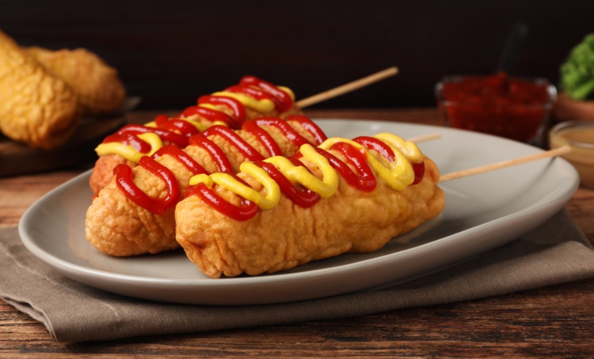 3 Corn Dogs mit Senf und Ketchup auf einem Teller.