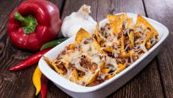 Überbackene Nachos mit Hackfleisch in der Auflaufform als Snack zum superbowl. Daneben liegen frische Zutaten.