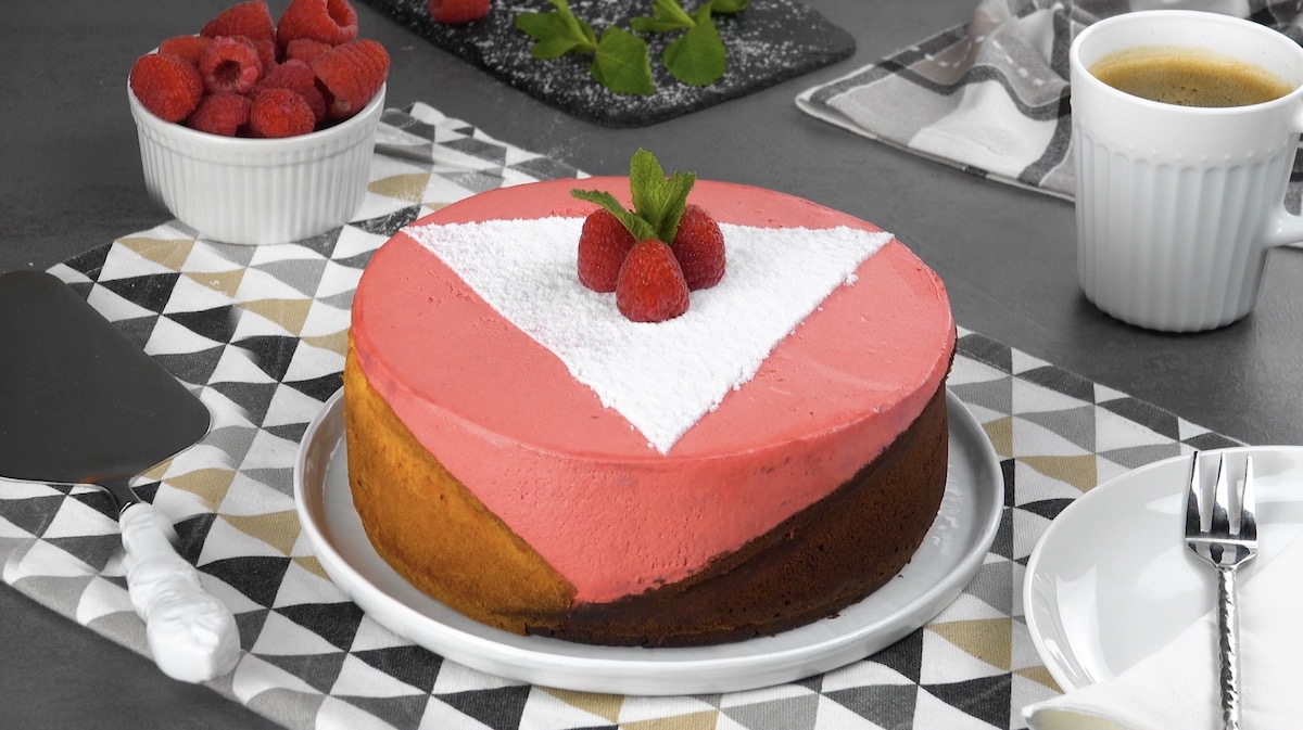 Schiefer Himbeerkuchen in geometrischem Design mit drei Farben, mit Himbeeren und Puderzucker sowie Minze dekoriert.