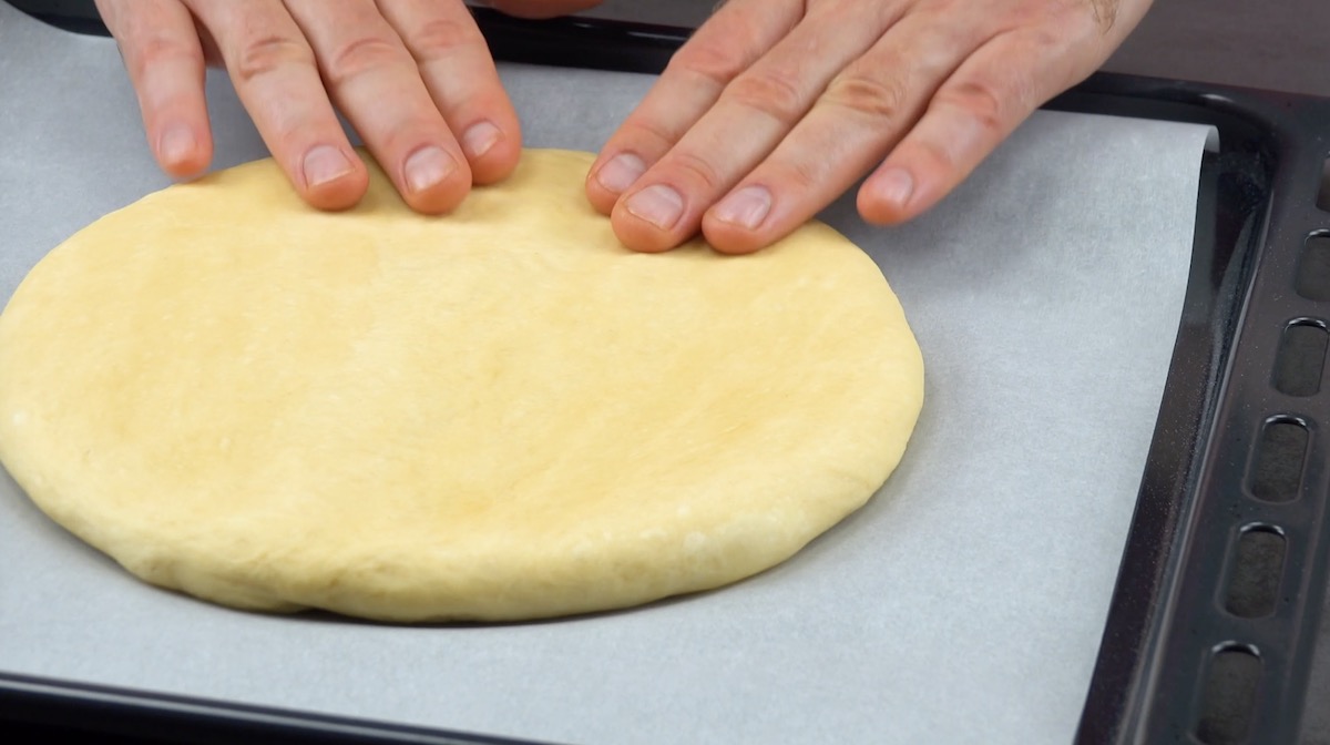 KreisfÃ¶rmig ausgerollter Teig auf einem mit Backpapier belegten Blech