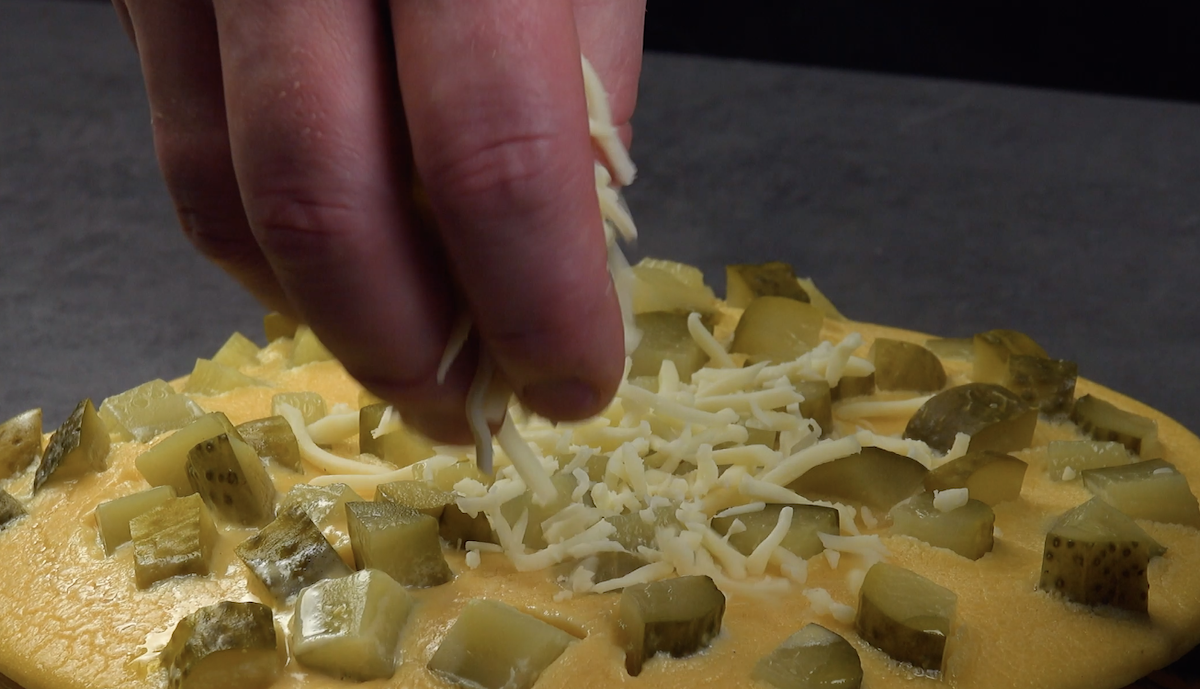 Ein Omelett-Pfannkuchen wird mit sauren Gurken und geriebenem KÃ¤se bestreut