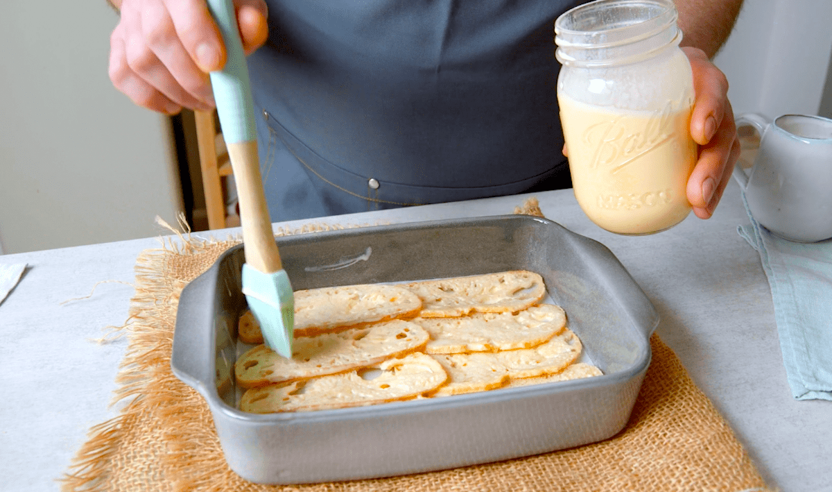 DÃ¼nne Brotscheiben liegen in einer Backform und werden mit einer Eier-Milch-Mischung bestrichen.