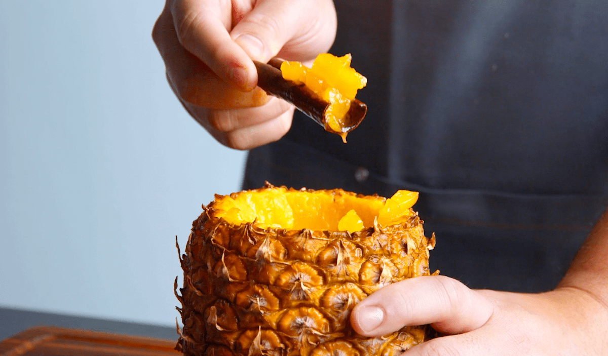 Das Fruchtfleisch aus einer gebackenen Ananas wird mit Zimtstangen herausgelÃ¶st.