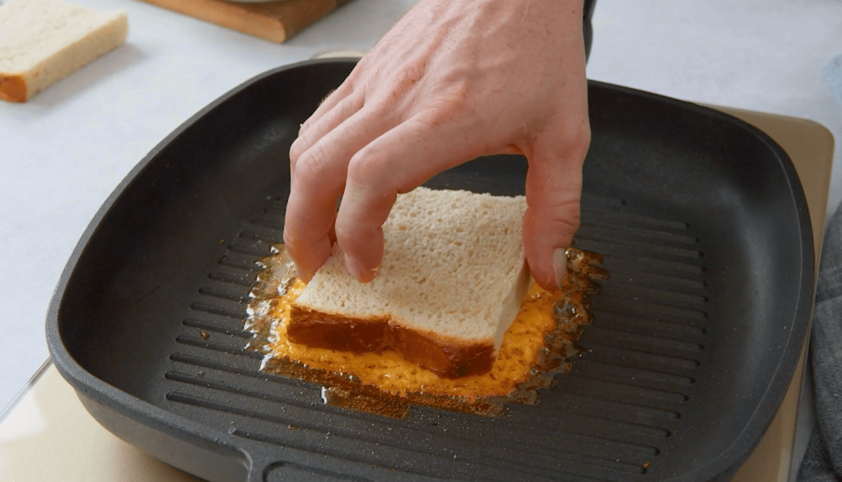 Eine Toastscheibe wird in geschmolzenen Cheddar in einer Pfanne gelegt