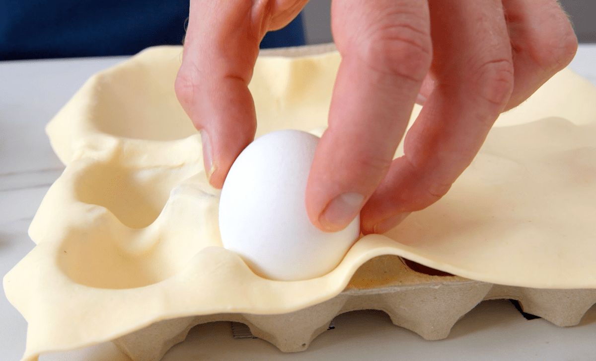 Ein Ei wird in BlÃ¤tterteig im Eierkarton gedrÃ¼ckt