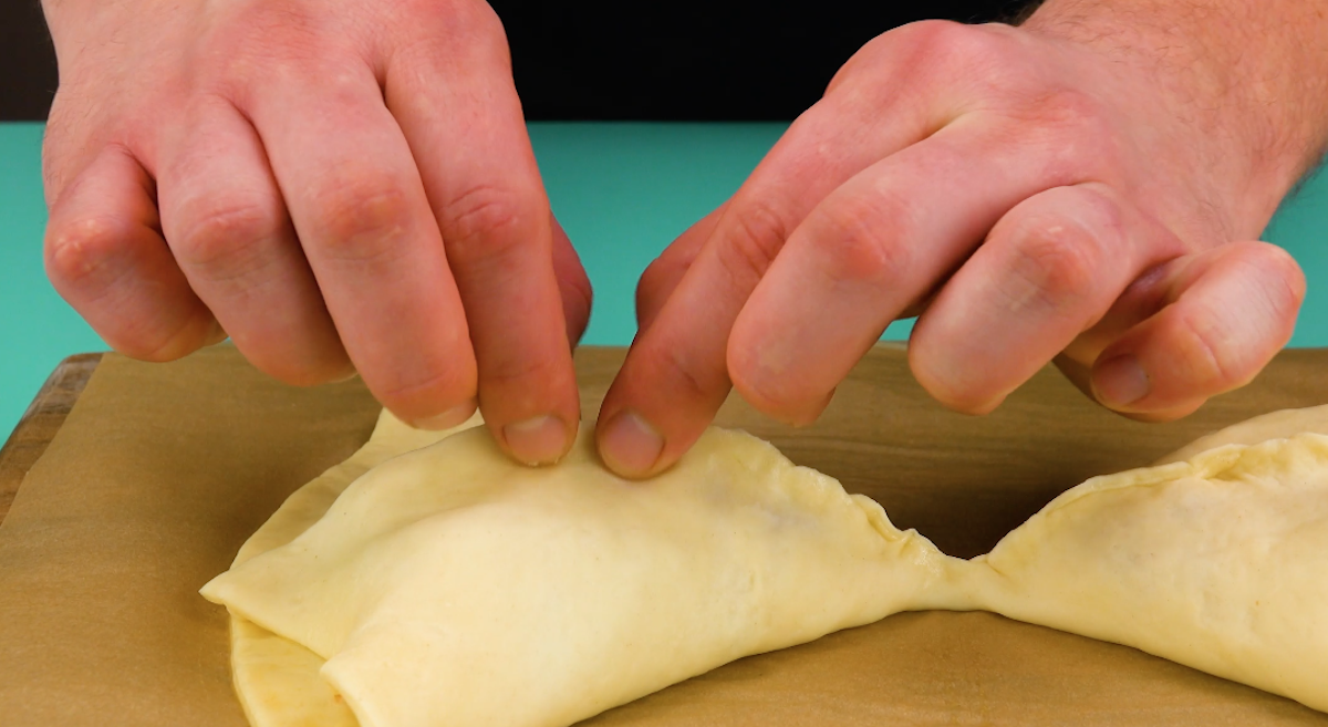 Pizzateig wird Ã¼ber FÃ¼llung geklappt und TeigrÃ¤nder zusammengedrÃ¼ckt.