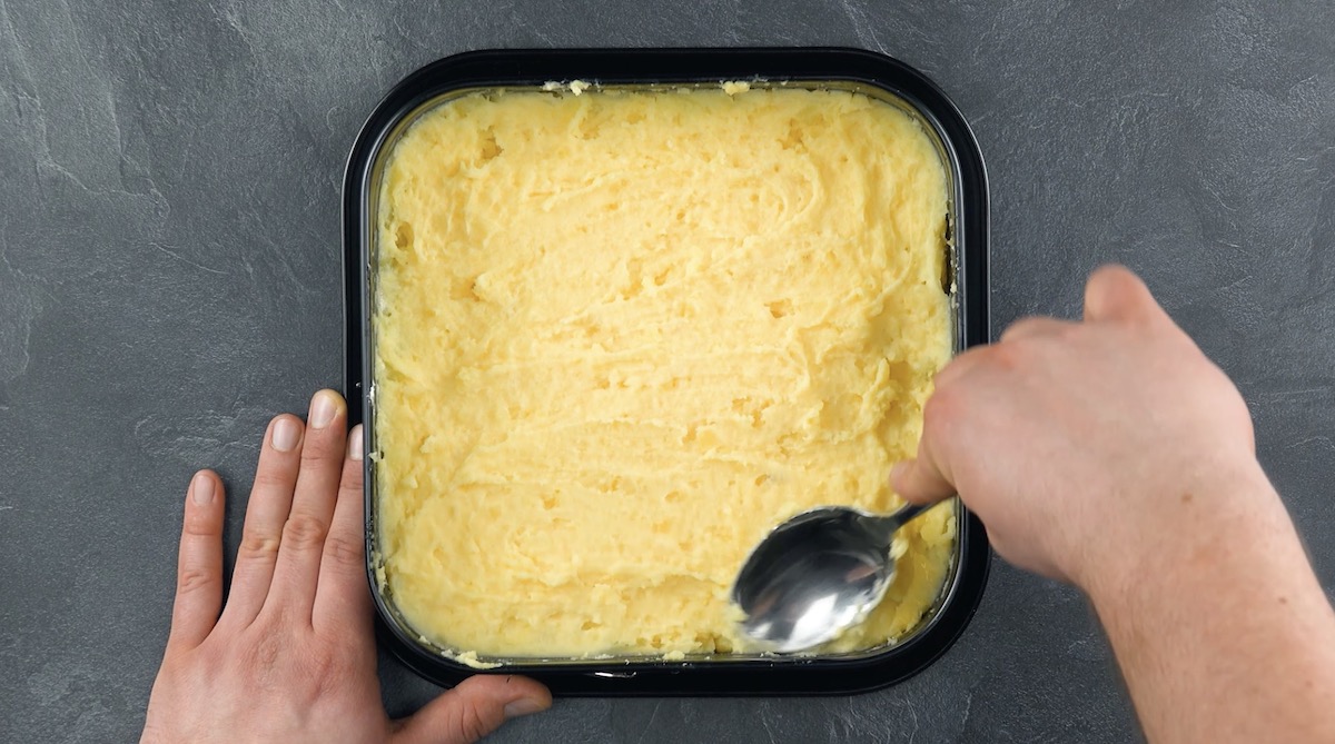 Kartoffelstampf wird auf dem Boden einer Kuchenform platt gestrichen