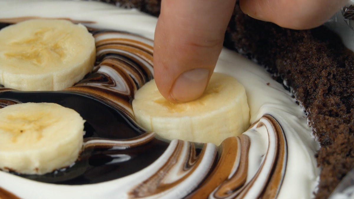 BananenstÃ¼cke werden in Creme hineingedrÃ¼ckt.