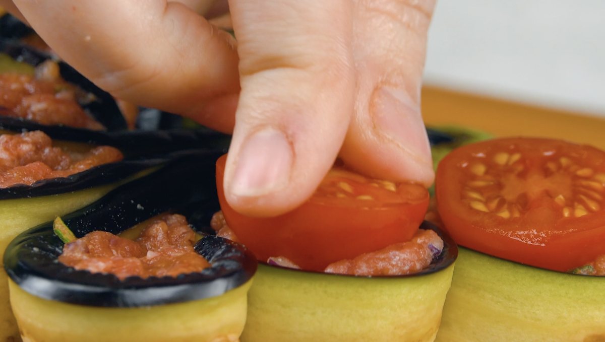 Halbe Kirschtomaten werden auf HackfÃ¼llung in Aubergine in Blumenform gelegt