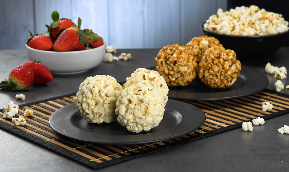 Zweierlei Popcorn-BÃ¤lle auf zwei Tellern, daneben eine Schale mit Erdbeeren und eine mit Popcorn