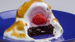 Gebackenes Eis mit Erdbeeren und Baiserhaube auf Teller, das angeschnitten wurde.