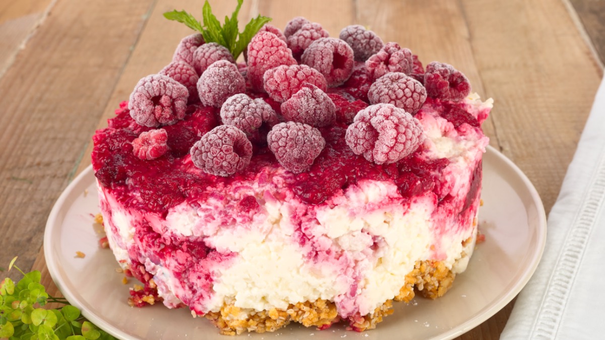 Eine Himbeerschnitte ohne Backen auf einem Teller mit Himbeeren als Garnitur.