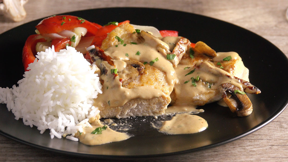 Eine Portion ParmesanhÃ¼hnchen mit cremiger Champignon-TomatensoÃŸe und Reis auf einem schwarzen Teller.