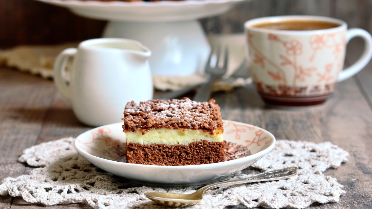 Ein Stück Schoko-Streuselkuchen, daneben eine Tasse Kaffee, ein Kännchen Milch und der restliche Kuchen.