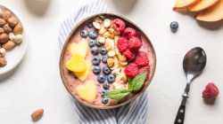 Ein bunte Smoothie-Bowl mit Porridge. Daneben liegen ein Löffel und frische Zutaten.