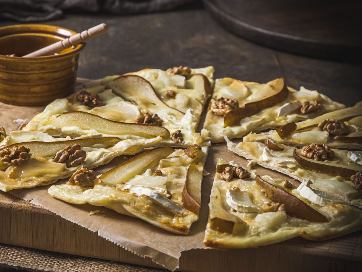 Flammkuchen mit Birne, Ziegenkäse und Walnüssen, in Scheiben geschnitten und serviert auf einem Holzbrett.