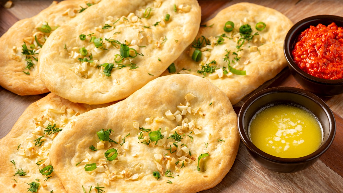 Naan-brote mit Knoblauch neben flÃ¼ssiger Butter und Dip in kleinen SchÃ¼sseln