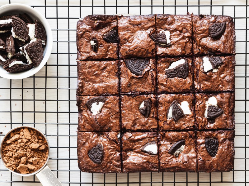 Oreo-Brownies auf einem Kuchengitter in der Draufsicht, daneben eine Schüssel mit zerkleinerten Oreos und eine mit Zucker.