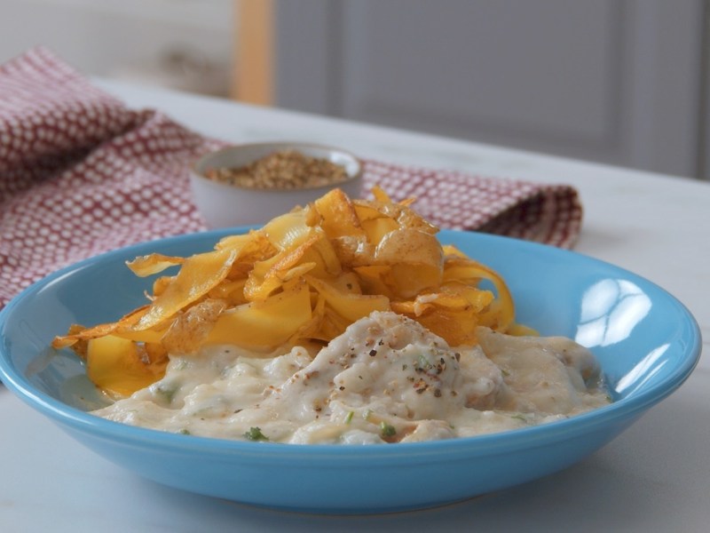 Schweinefilet in Blumenkohlsoße mit Kartoffelnudeln, serviert auf einem blauen Teller.
