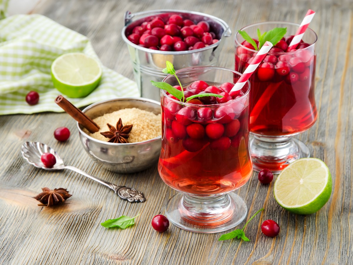 2 GlÃ¤ser Cranberry Paloma mit Cranberrys und Strohhalm, drumherum Zutaten wie Zucker, Cranberrys, Anis und Zimtstangen.