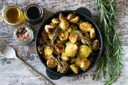 Gebackener Rosenkohl mit Balsamico und Ahornsirup in einer gusseisernen Form in der Draufsicht, daneben Gläser mit Zutaten und Rosmarin.