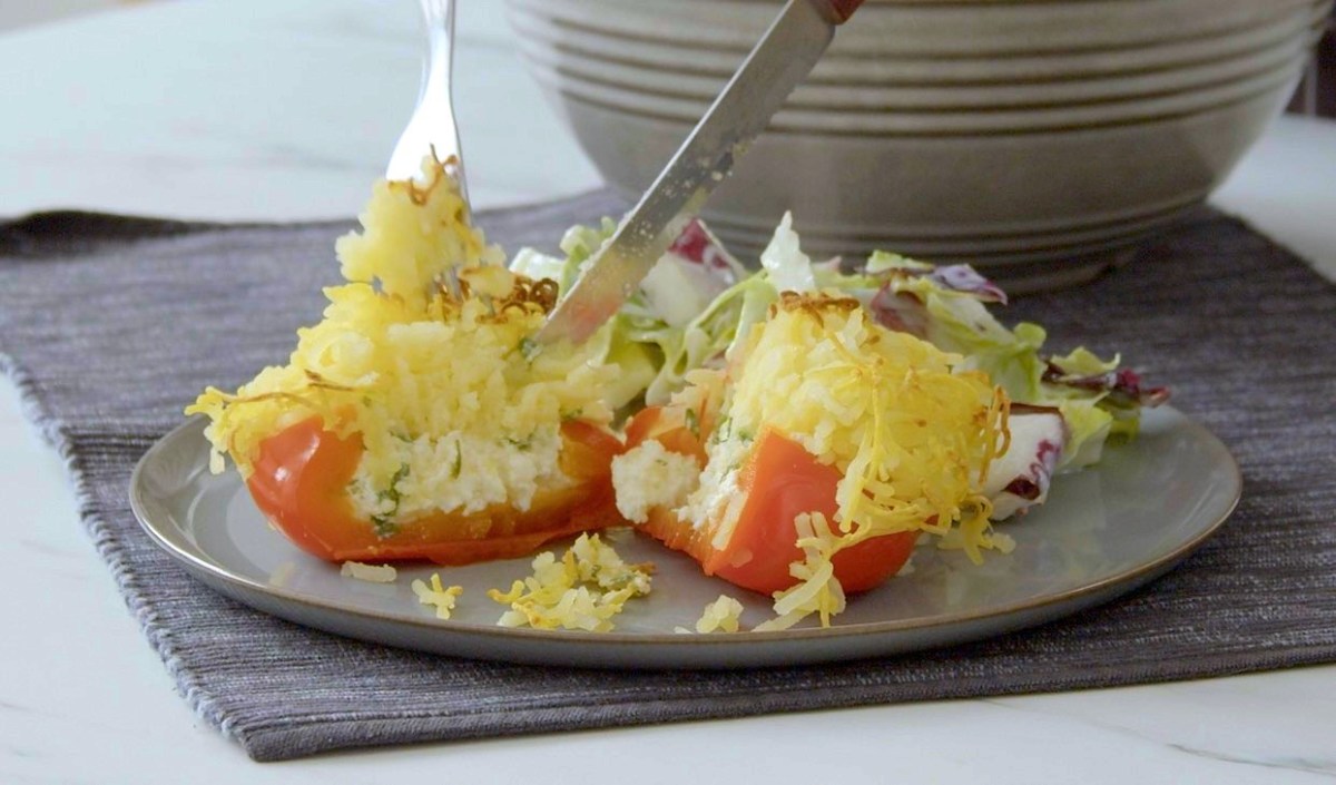 Eine angeschnittene gefüllte Paprika mit Kartoffelhaube und Feta gefüllt auf einem Teller.