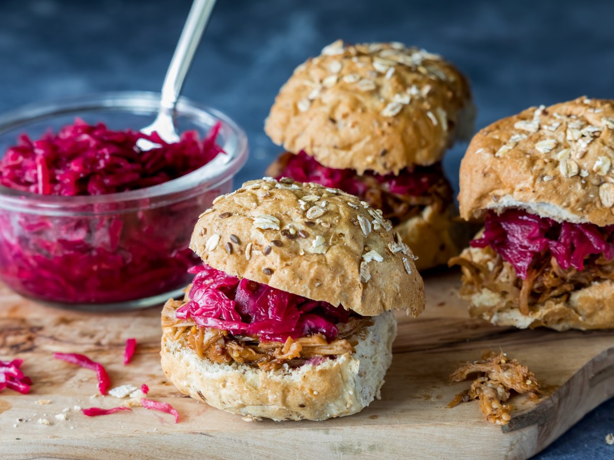 3 kleine Rotkohl-Gänse-Burger auf einem Brett, auf dem auch eine Glasschüssel mit Rotkohl steht.