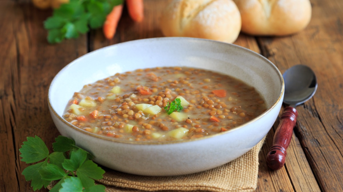 Eine Schüssel mit Omas Linsensuppe. Daneben liegen ein Löffel und einige der Zutaten.