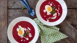 Zwei Schüsseln mit Rote-Bete-Suppe. Daneben ein Geschirrtuch und Löffel.