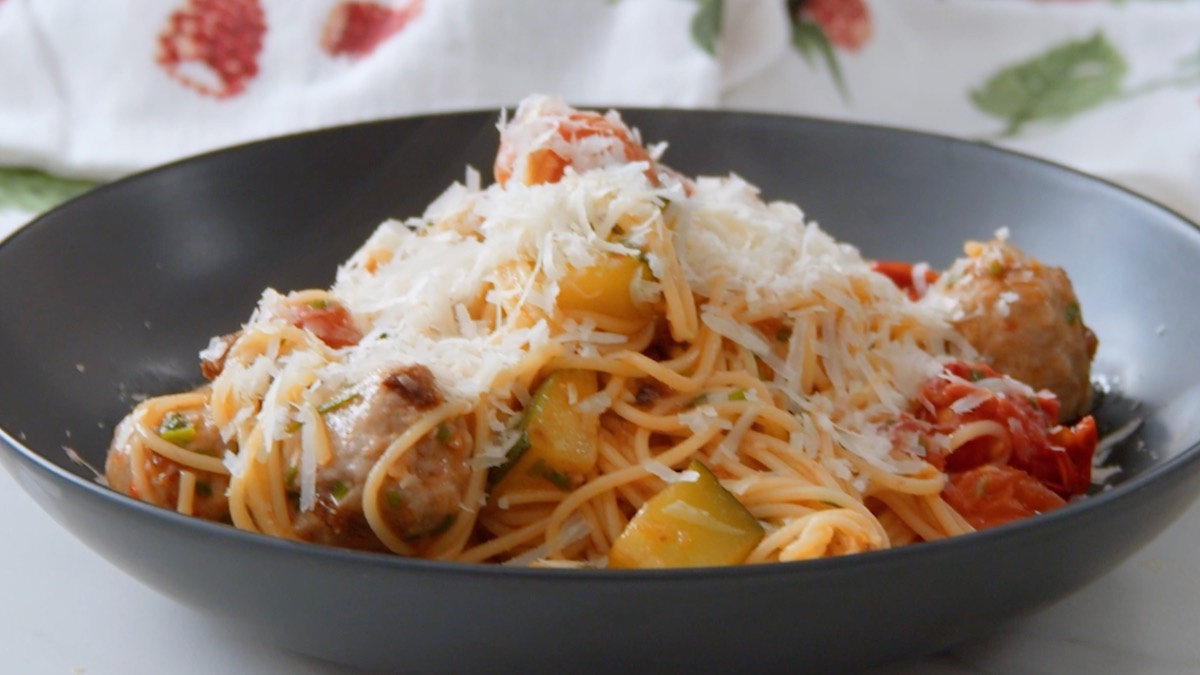 Ein schqarzer Teller mit einer Pasta-Pfanne mit Fleischbällchen, Gemüse und geriebenem Parmesan.