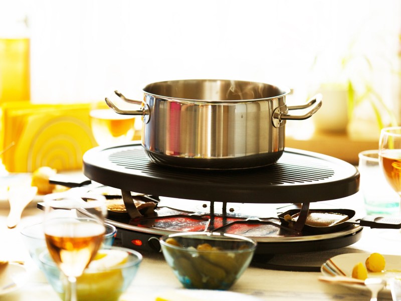 Süßes Raclette: Ein Raclette-Grill auf einem reich gedeckten Tisch, auf dem Grill steht ein silberner Topf.