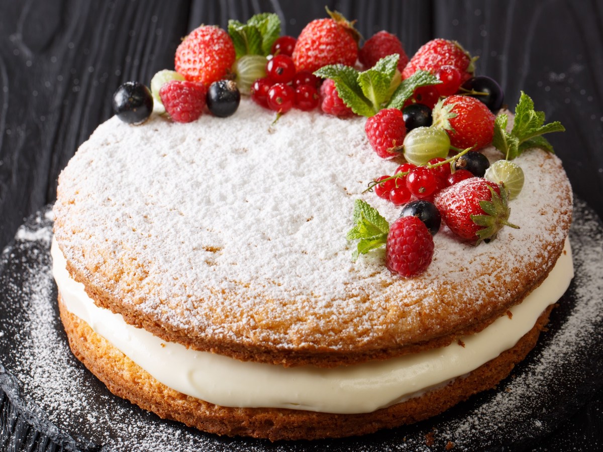 Ein Victoria Sponge Cake mit Creme, mit Puderzucker bestreut und frischen Beeren garniert.