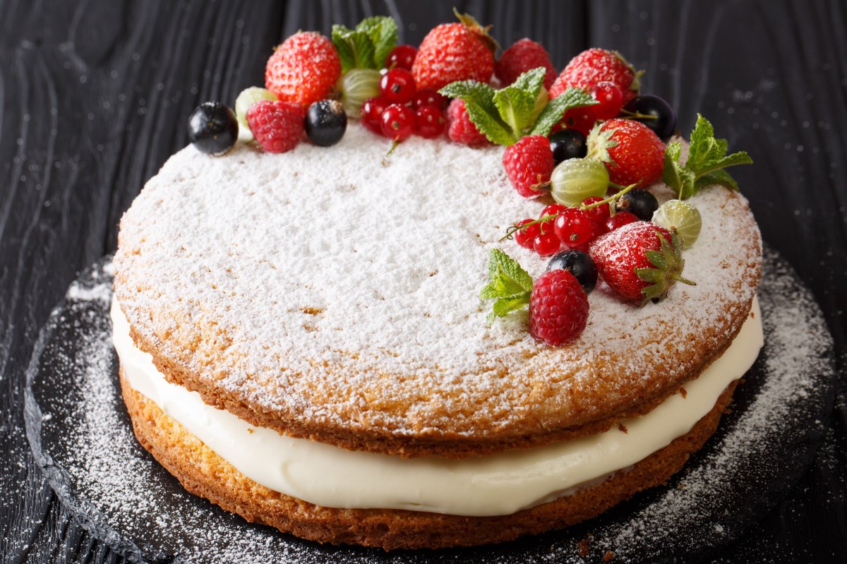 Ein Victoria Sponge Cake mit Creme, mit Puderzucker bestreut und frischen Beeren garniert.