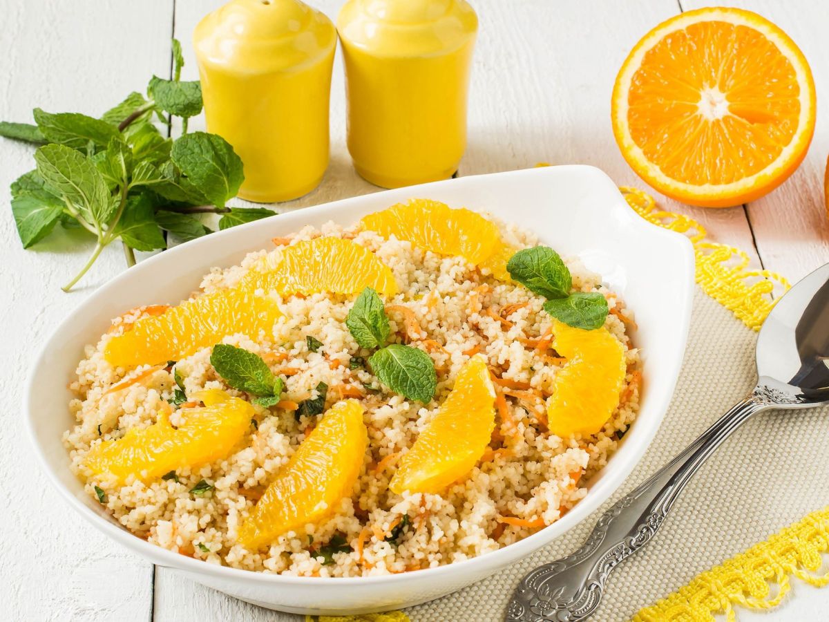 Bulgur-Orangen-Bowl, serviert in einer SchÃ¼ssel. Orangenscheiben und Minze als Deko. Salz- und Pfefferstreuer sowie frische Minze und eine aufgeschnittene Orange stehen als Dekoration neben und hinter der SchÃ¼sse.