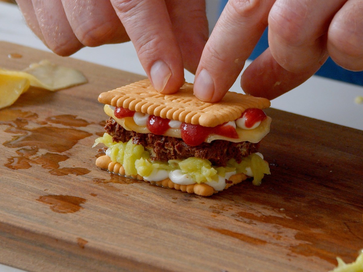 Ein kleines Butterkeks-Sandwich mit Sahne, Obst, Himbeersoße und Schokolade auf einem Brett.