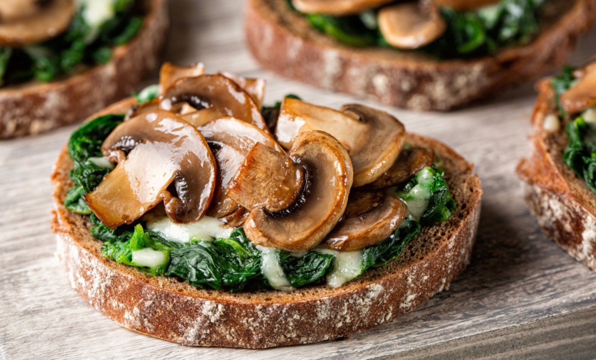 Mehrere Portionen Champignon-Bruschetta mit Ricotta und frischen Kräutern.