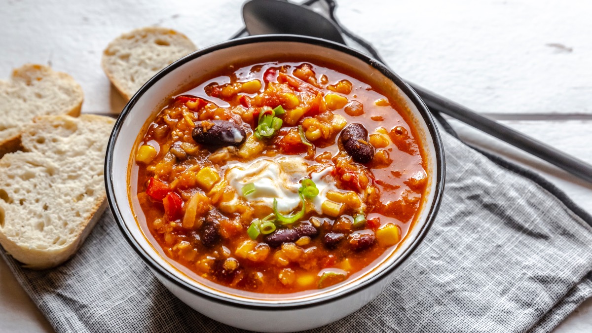 Eine Schüssel mit Chili sin Carne auf einer Stoffserviette. Daneben liegen Brotscheiben und ein Löffel.