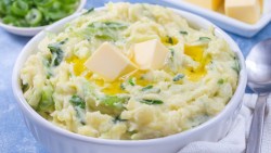 Eine Schüssel mit Colcannon. Daneben liegen ein Löffel und mehrer schalen mit Zutaten.