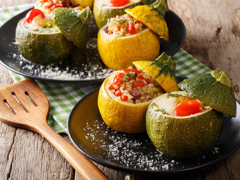 Gefüllte Zucchini mit Bulgur und Tomaten auf einem schwarzen Teller, garniert mit etwas Dill