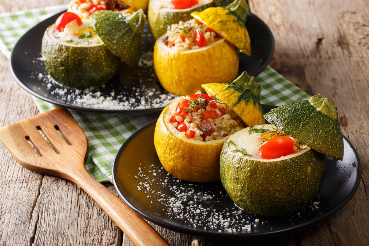 Gefüllte Zucchini mit Bulgur und Tomaten auf einem schwarzen Teller, garniert mit etwas Dill