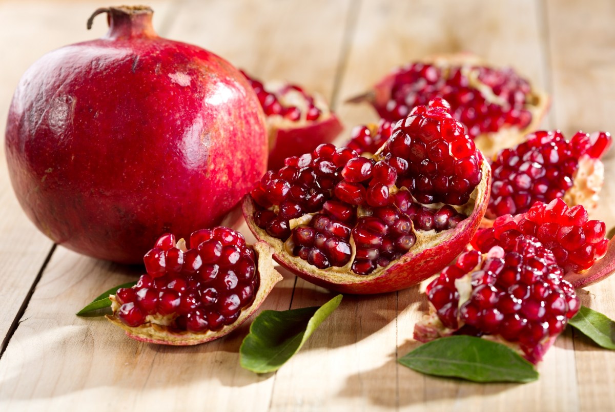 Granatapfel entkernen: ein ganzer und ein geöffneter Granatapfel auf Holz.