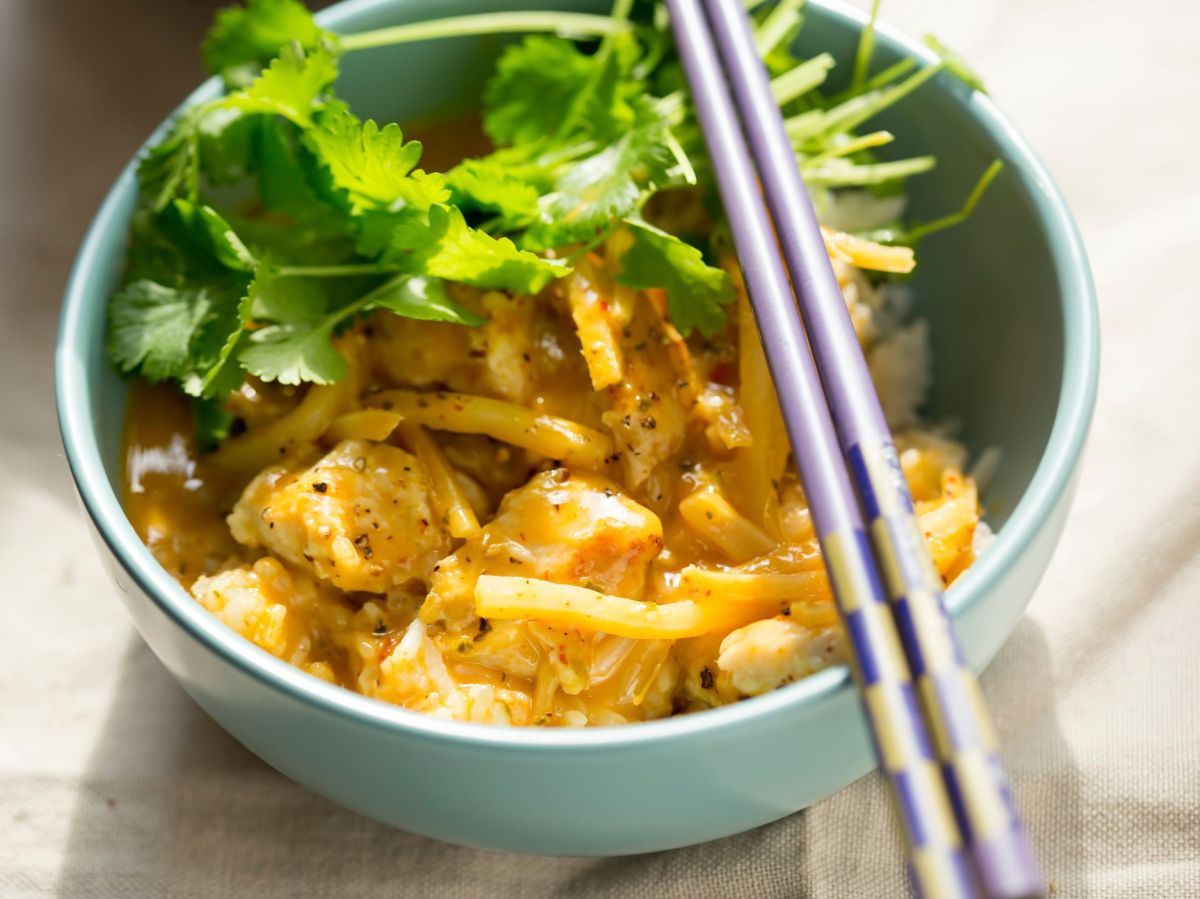 Mango-Curry, serviert in einer großen Schale. Stäbchen und Koriander liegen als Deko auf und neben der Schüssel.