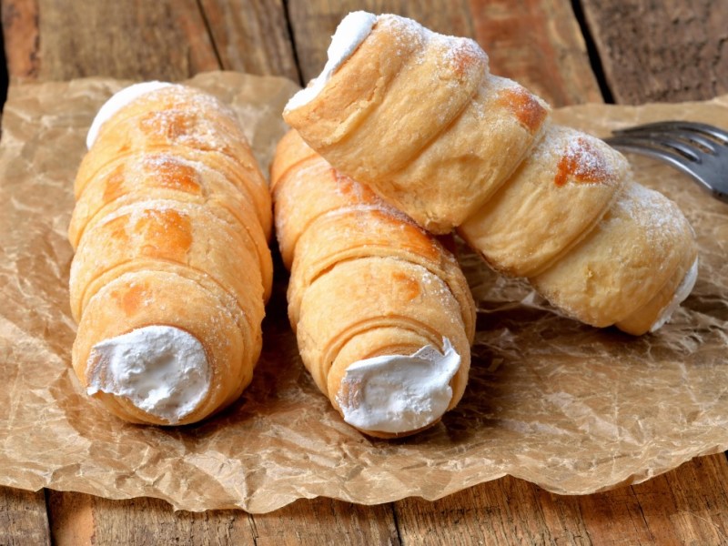 Drei Schaumrollen mit Vanillecreme auf einem Stück Backpapier.